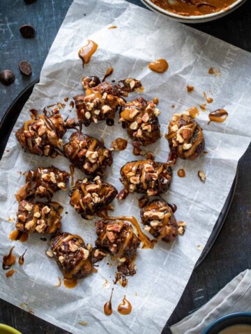 Stuffed dates topped with caramel and chocolate on a piece of parchment paper laying on a black plate