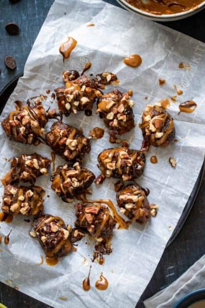 Stuffed dates topped with caramel and chocolate on a piece of parchment paper laying on a black plate