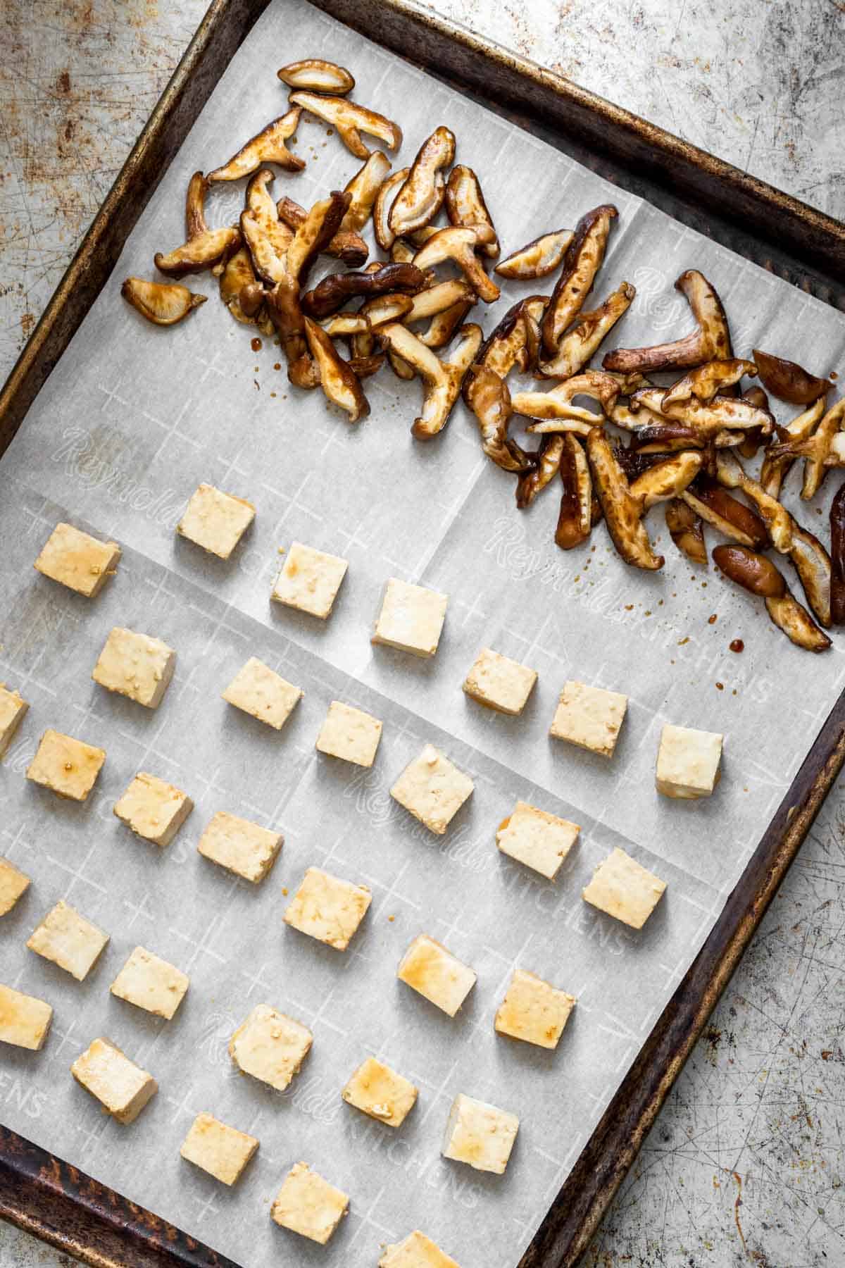 A parchment lined baking sheet with cubes of tofu and sliced shiitake mushrooms