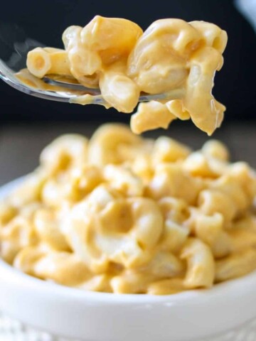 A fork with a bit of mac and cheese on it over a bowl of more