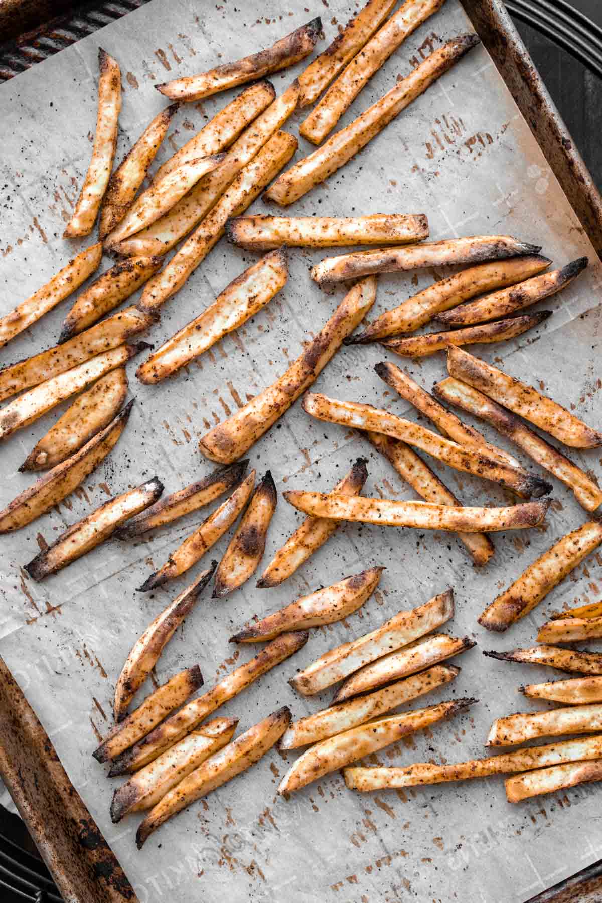 A pan with parchment paper and baked sweet potato fries covered in seasoning.
