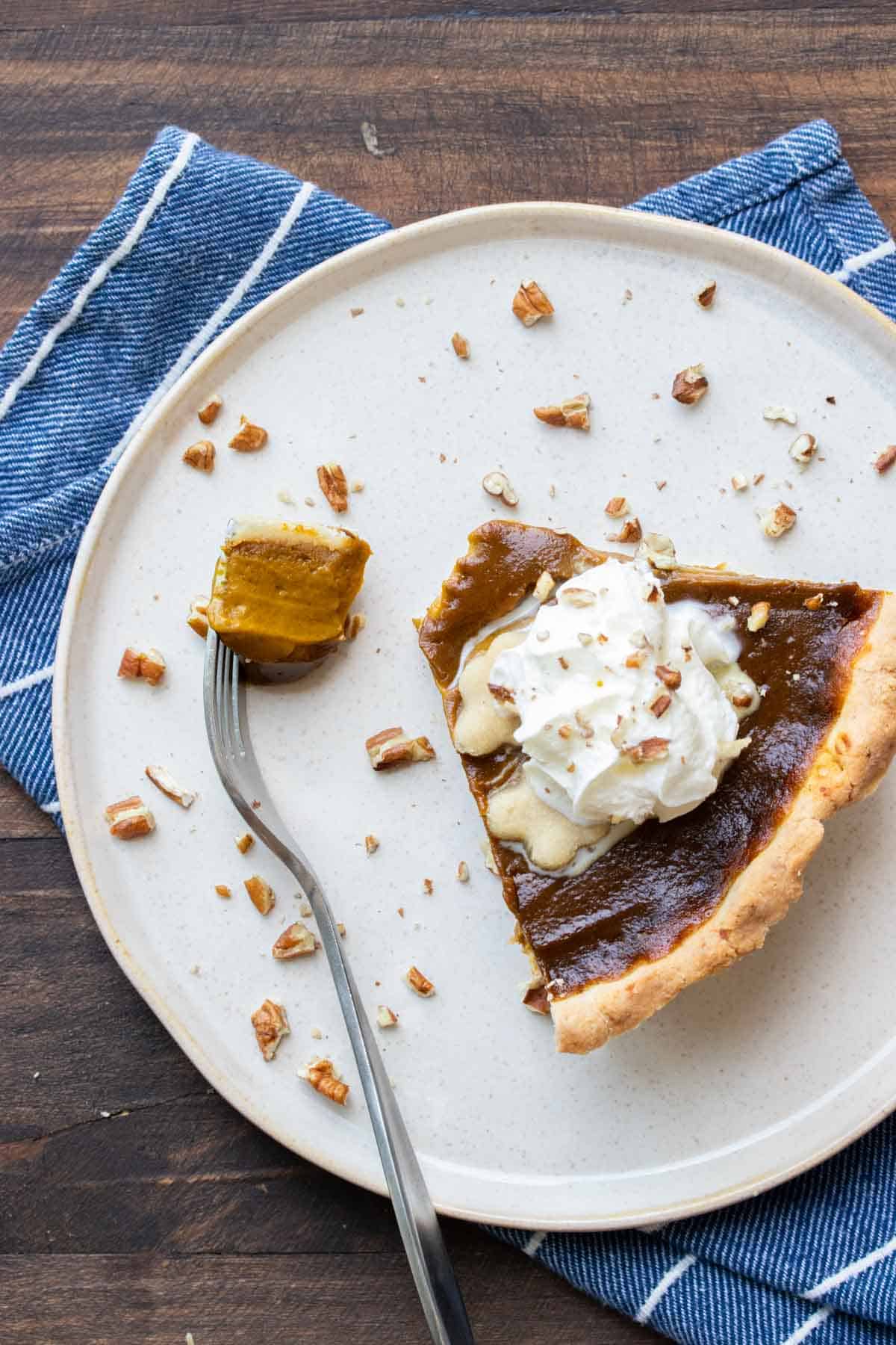 Top view of a slice of whipped cream topped pumpkin pie on a white plate with a bite on a fork.