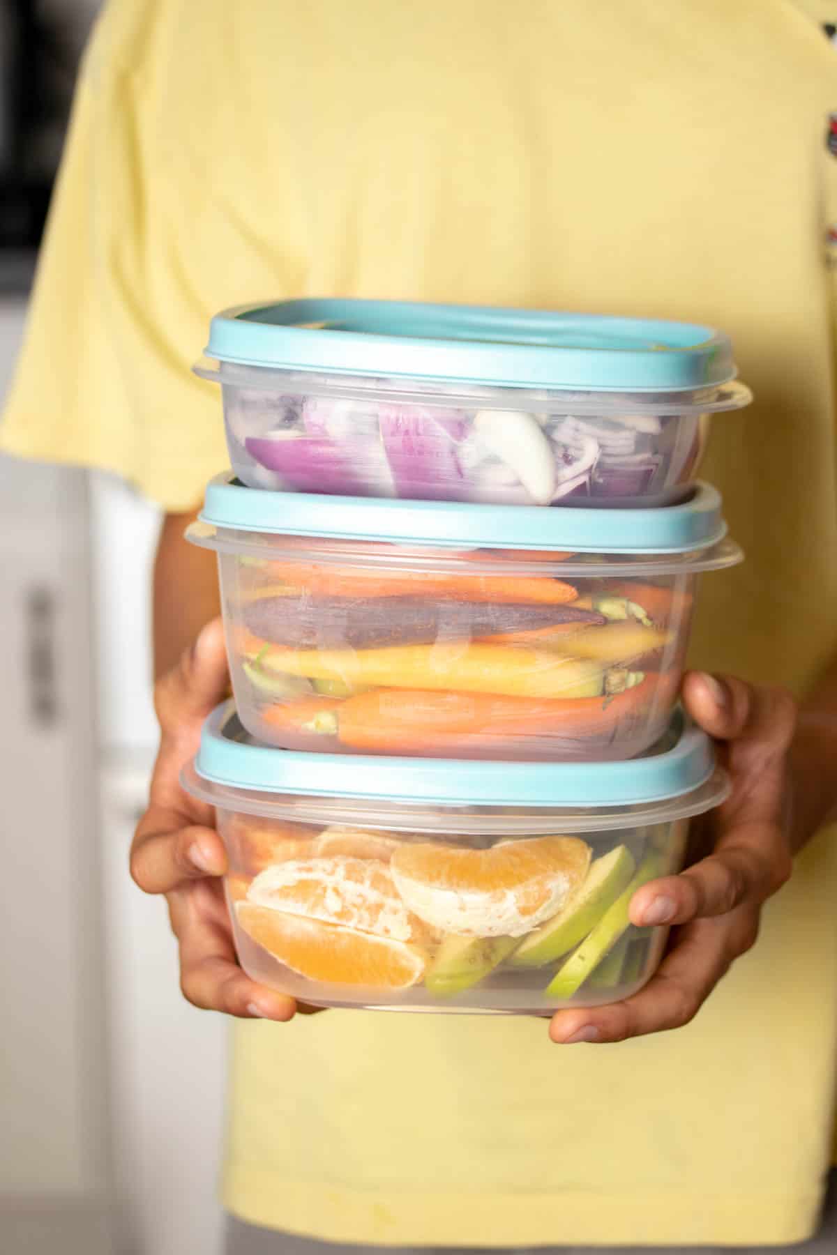 Hands of a person wearing a yellow shirt holding a stack of three containers with blue lids.