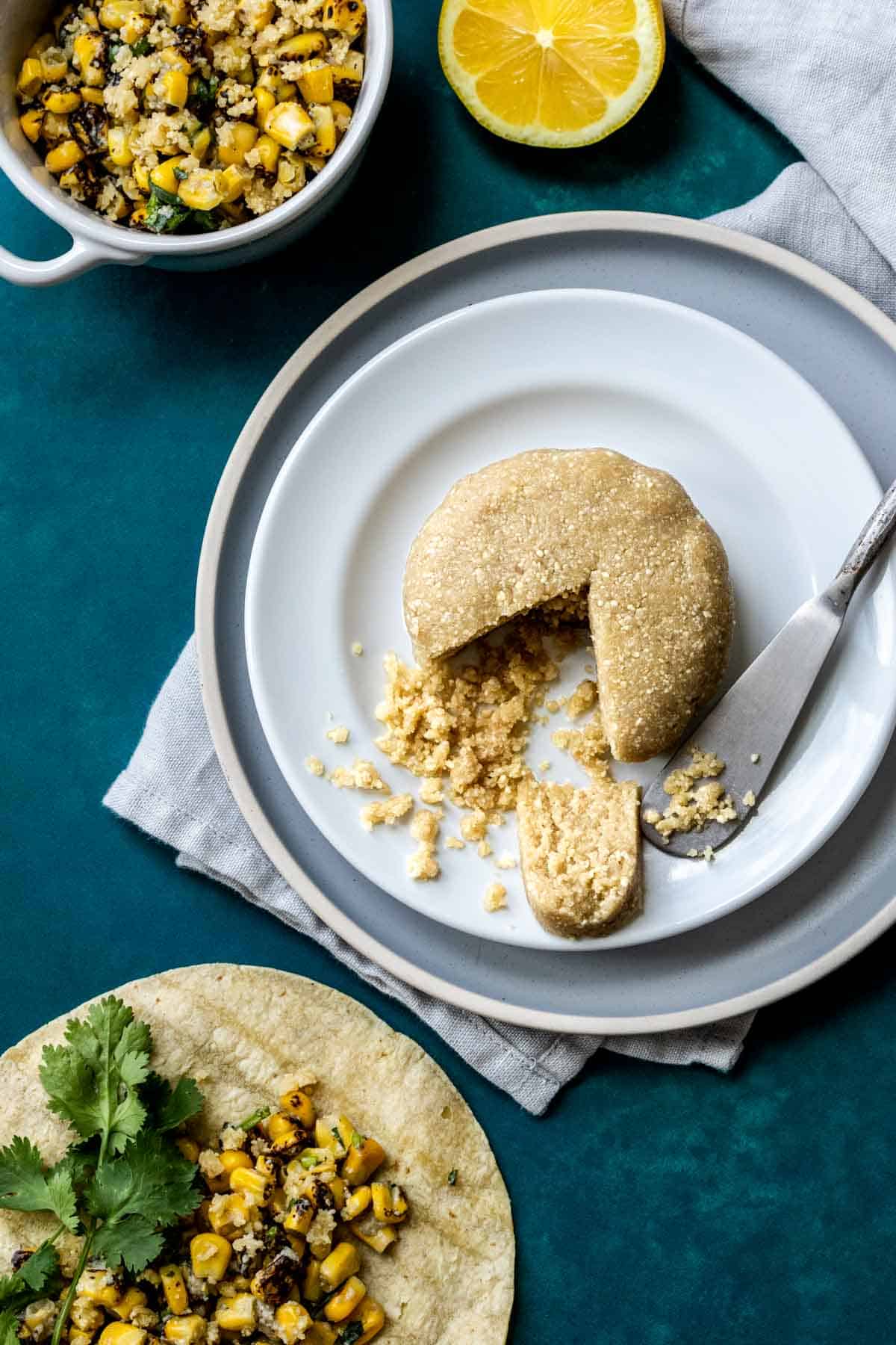 Top view of a white plate stacked on a grey plate and a wheel of nut based cheese with a triangle cut out.