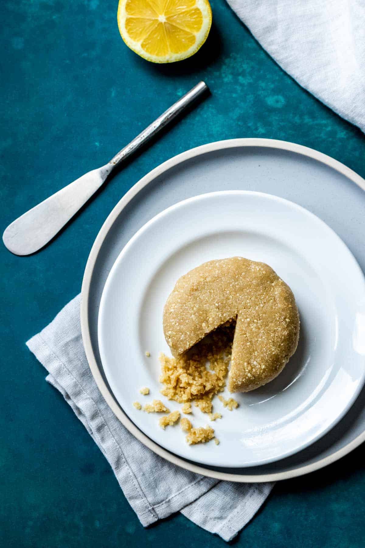 A grey plate with a white plate on it and a nut based cheese wheel with a triangle slice out of it on the plate.