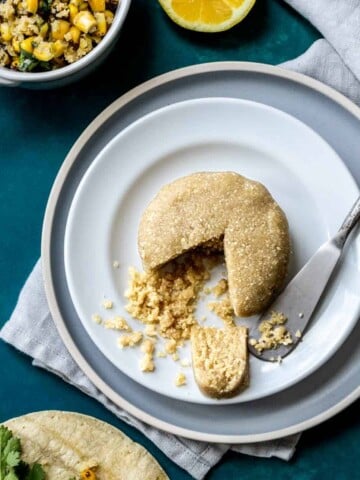 A stack of two plates on a dark turquoise surface with a nut based cheese wheel on them and a slices out of it.