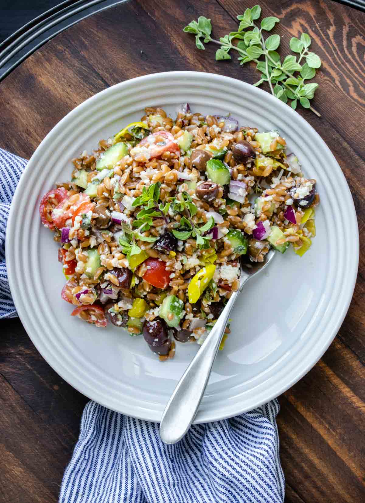 A fork in a pile of farro with Greek themed ingredients mixed in on a white plate