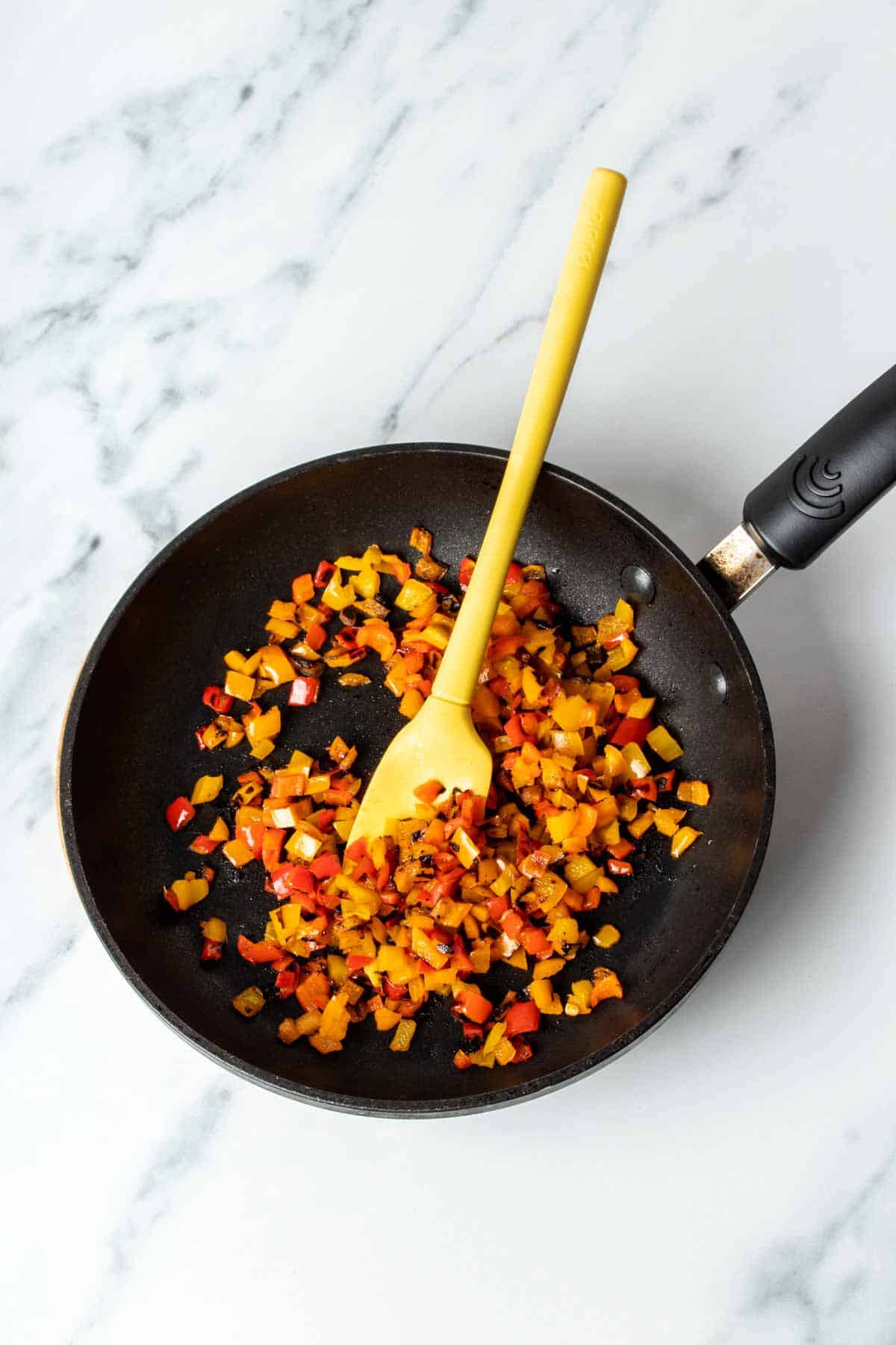 A yellow spatula mixing cooked chopped peppers in a black pan.