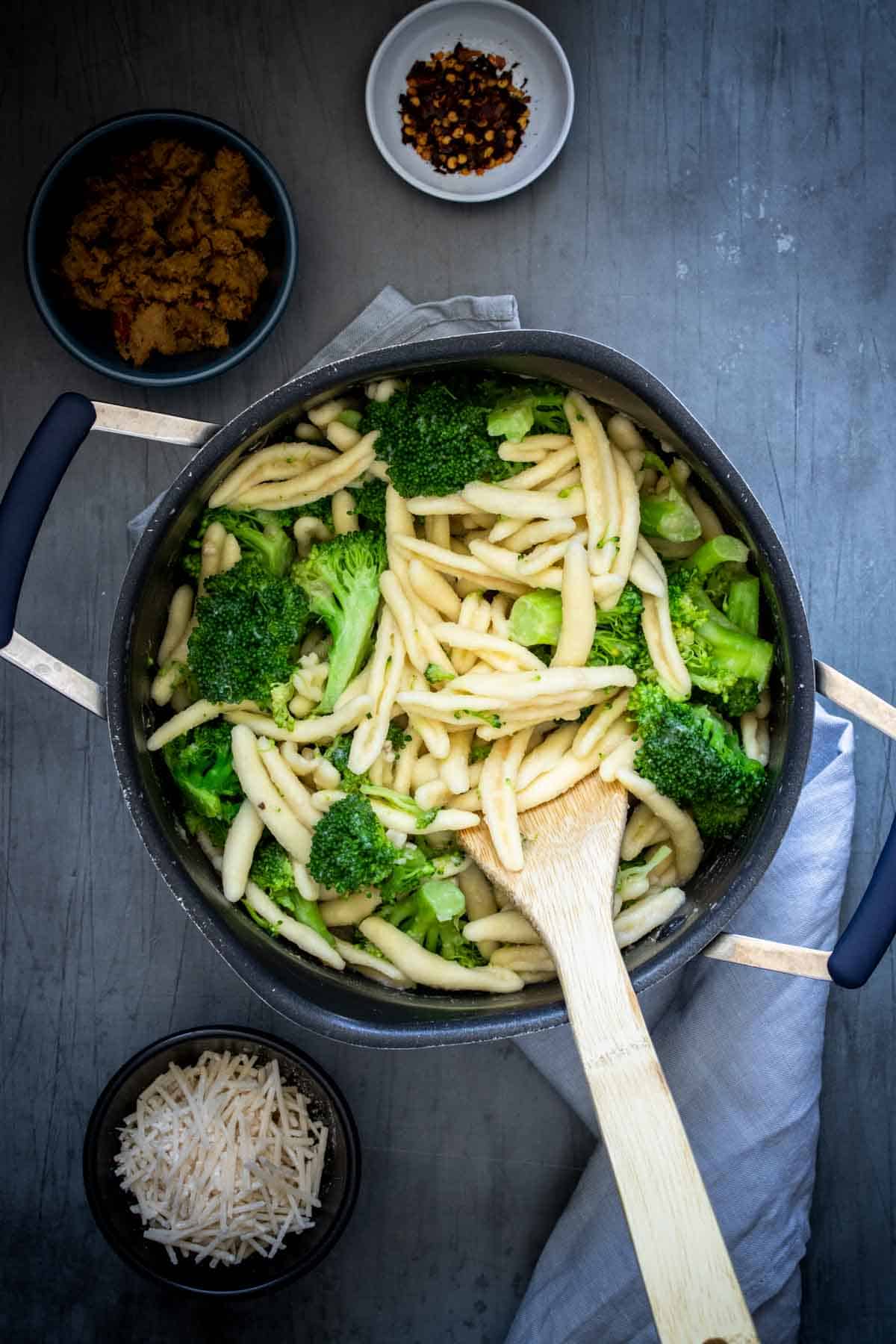 Cavatelli pasta being mixed with broccoli by a wooden spoon in a pot