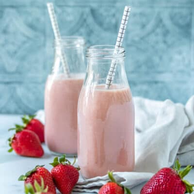 Pink strawberry milk in two glass jars with straws sitting in front of each other around strawberries