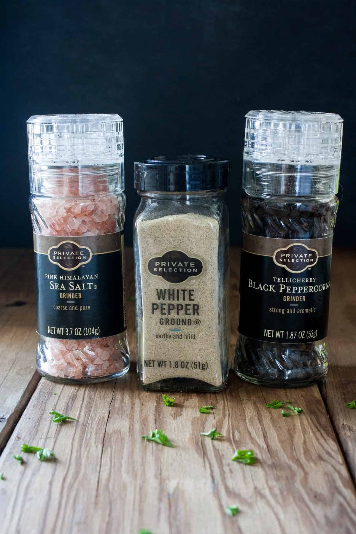 A jar of pink salt, white pepper and black peppercorns sitting on a wooden surface.