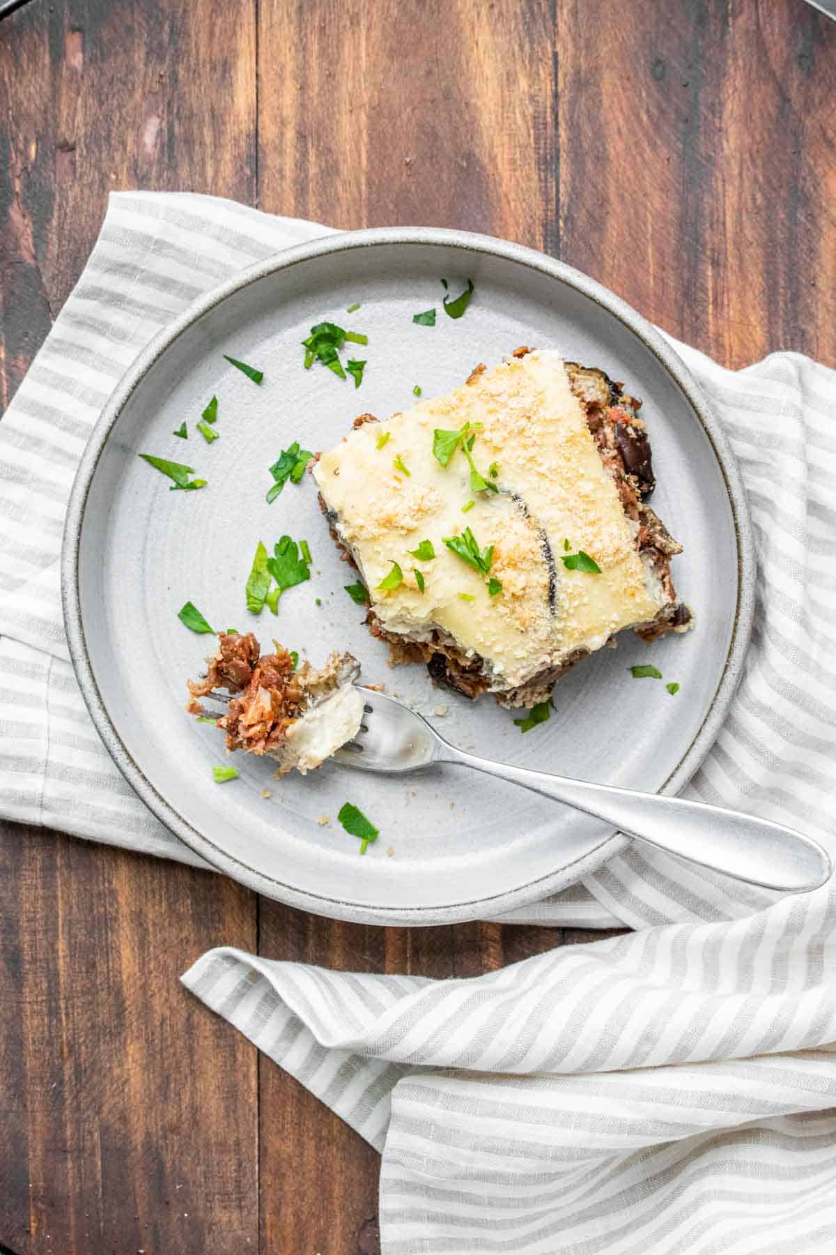 Top view of a grey plate with a piece of moussaka on it and a fork with a bite on the plate.