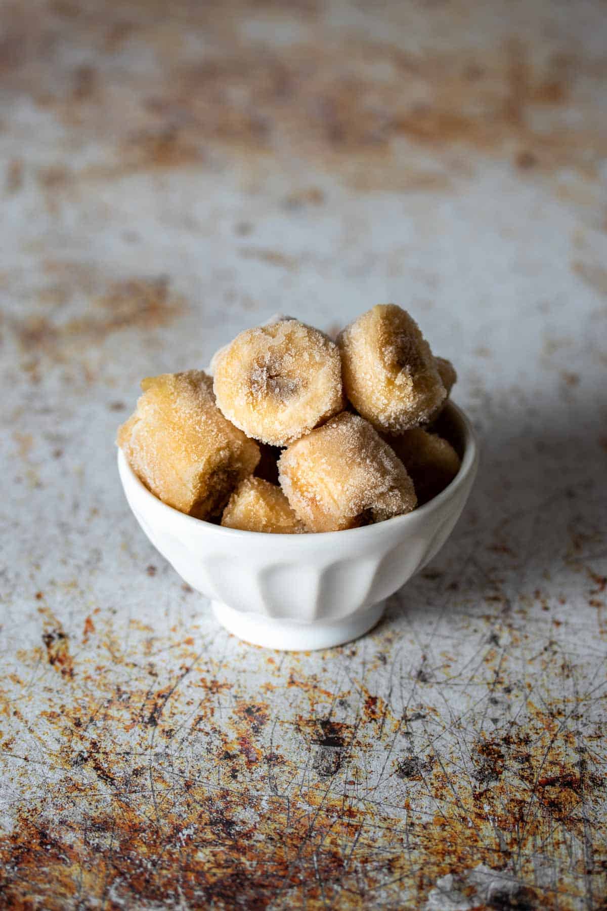 A white bowl on a brown and white surface filled with slices of frozen bananas.