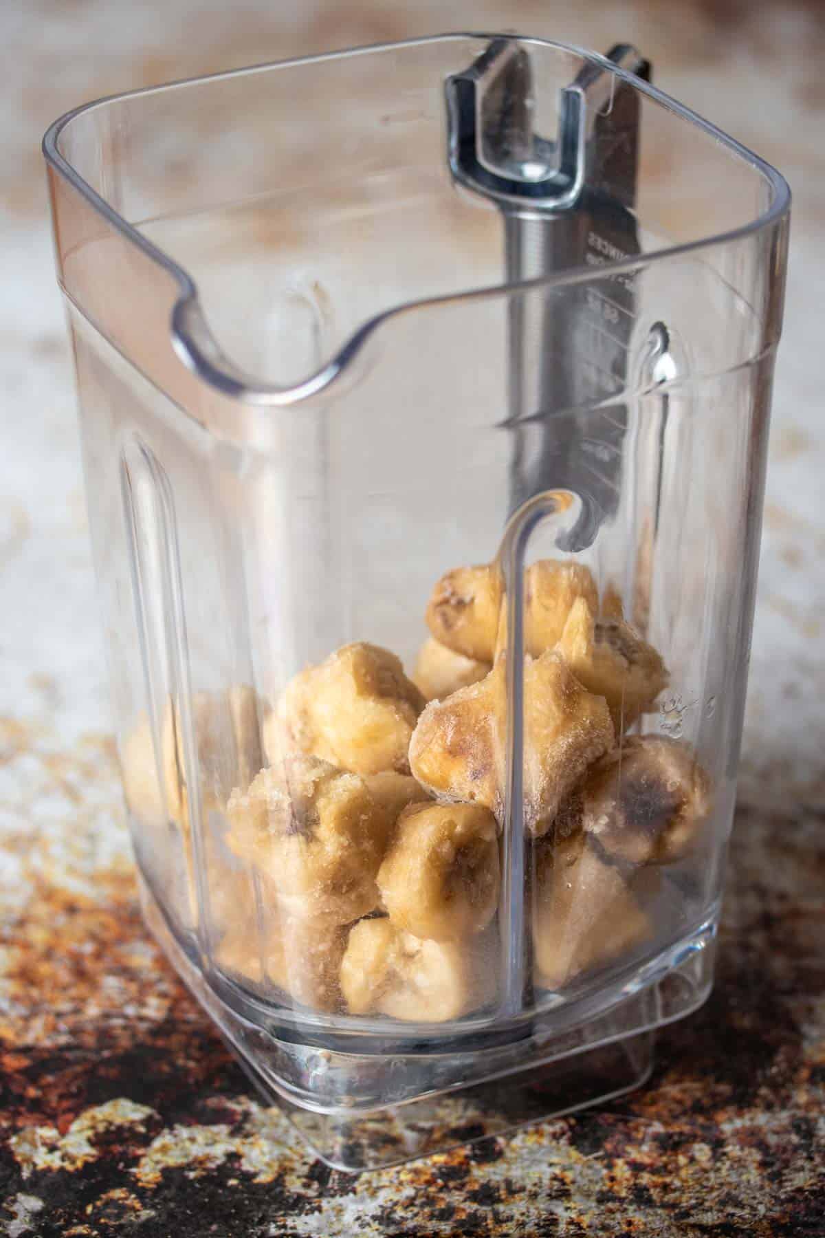 A blender with frozen slices of bananas inside it on top of a brown and white surface.