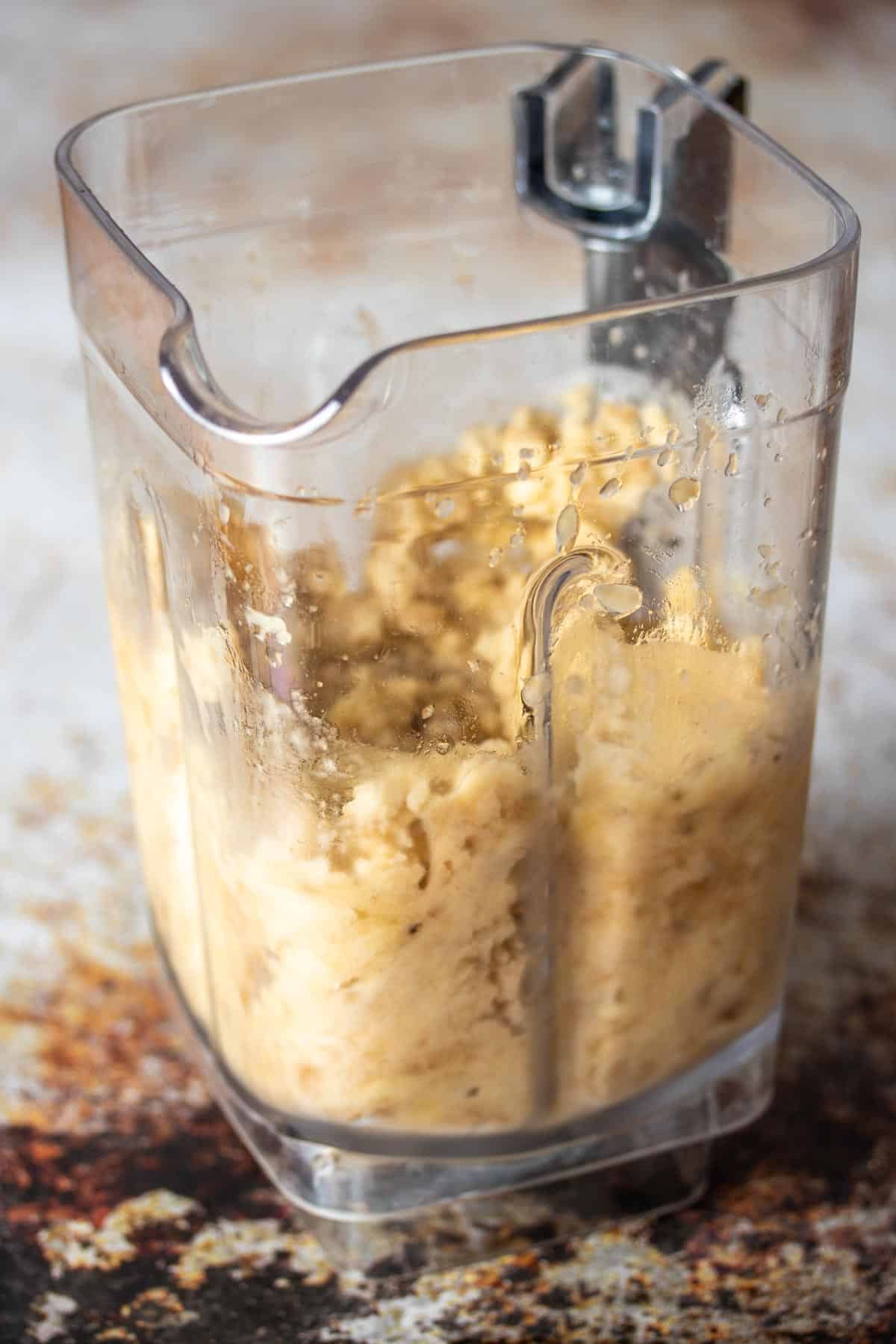 A blender with pulsed frozen bananas inside it sitting on a brown and white surface.