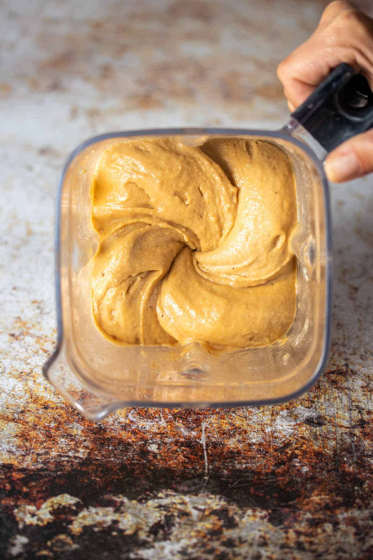 A hand holding a blender so you can see blended peanut butter ice cream inside it.