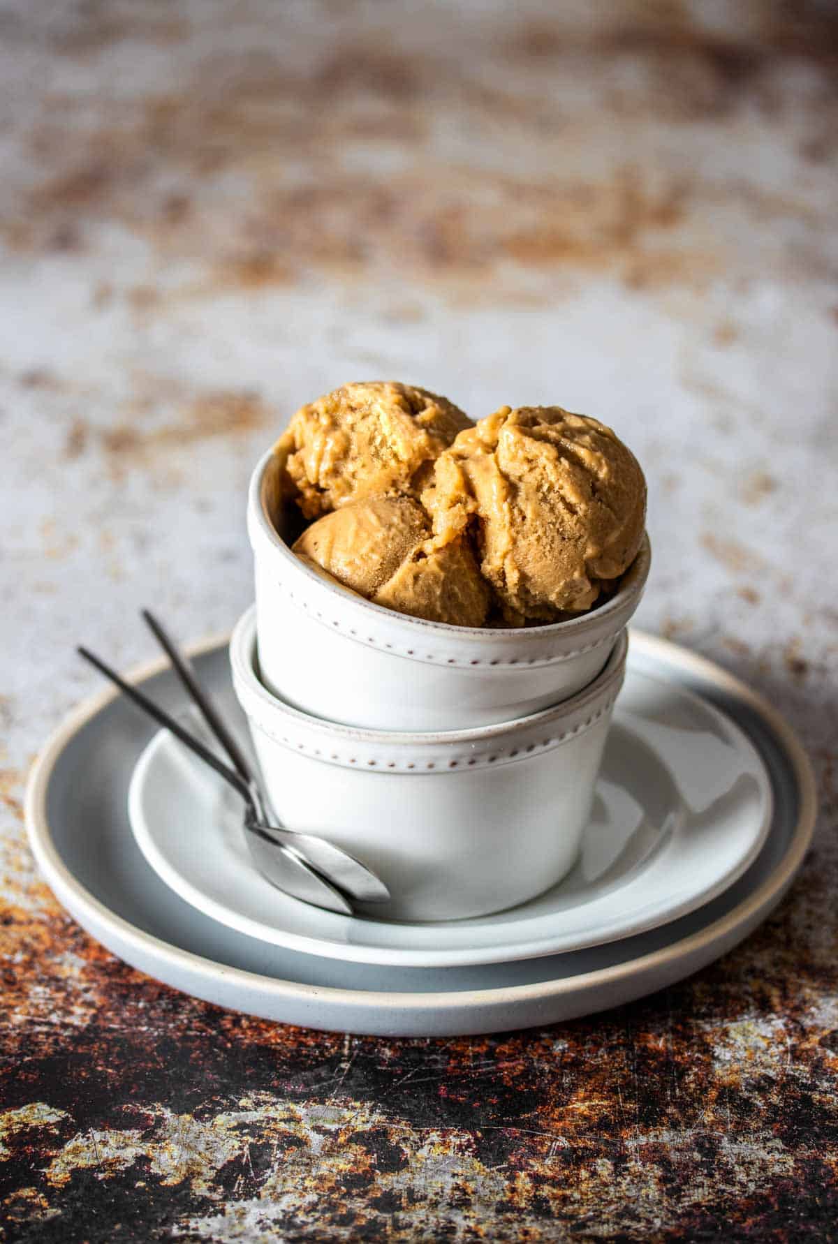 Three scoops of peanut butter ice cream inside a white bowls stacked on another bowl and on two stacked white plates