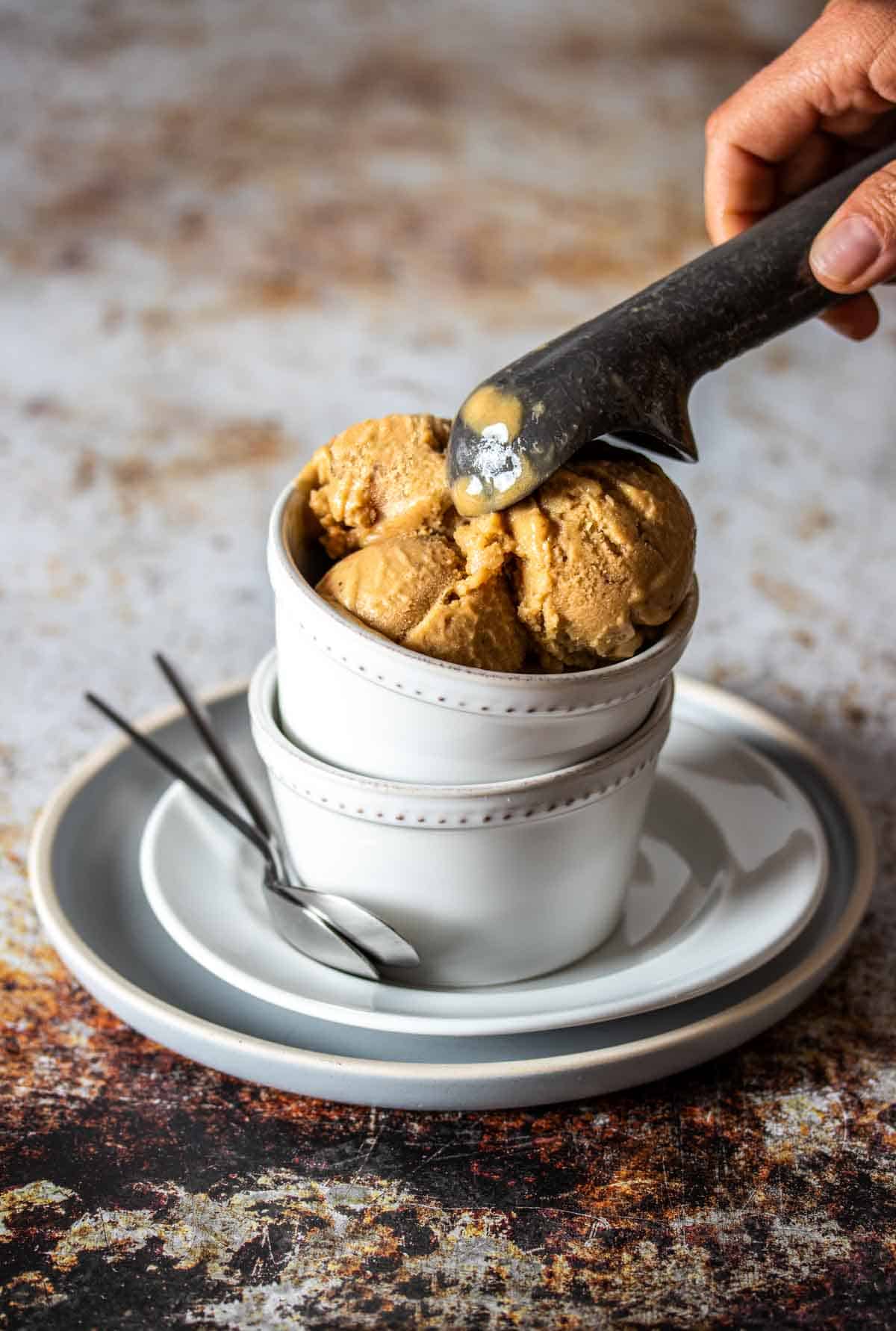 An ice cream scooper putting peanut butter ice cream in a white bowl stacked on another bowl.