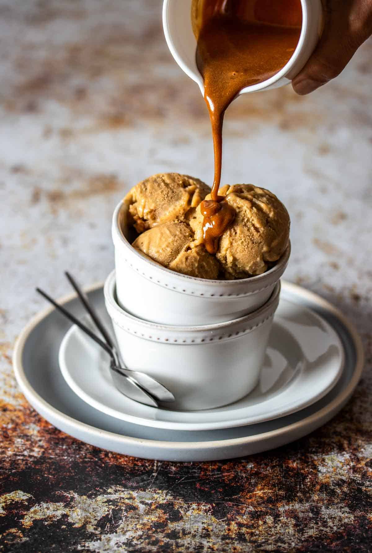 White bowls stacked on each other with scoops of peanut butter ice cream and caramel drizzling on it.