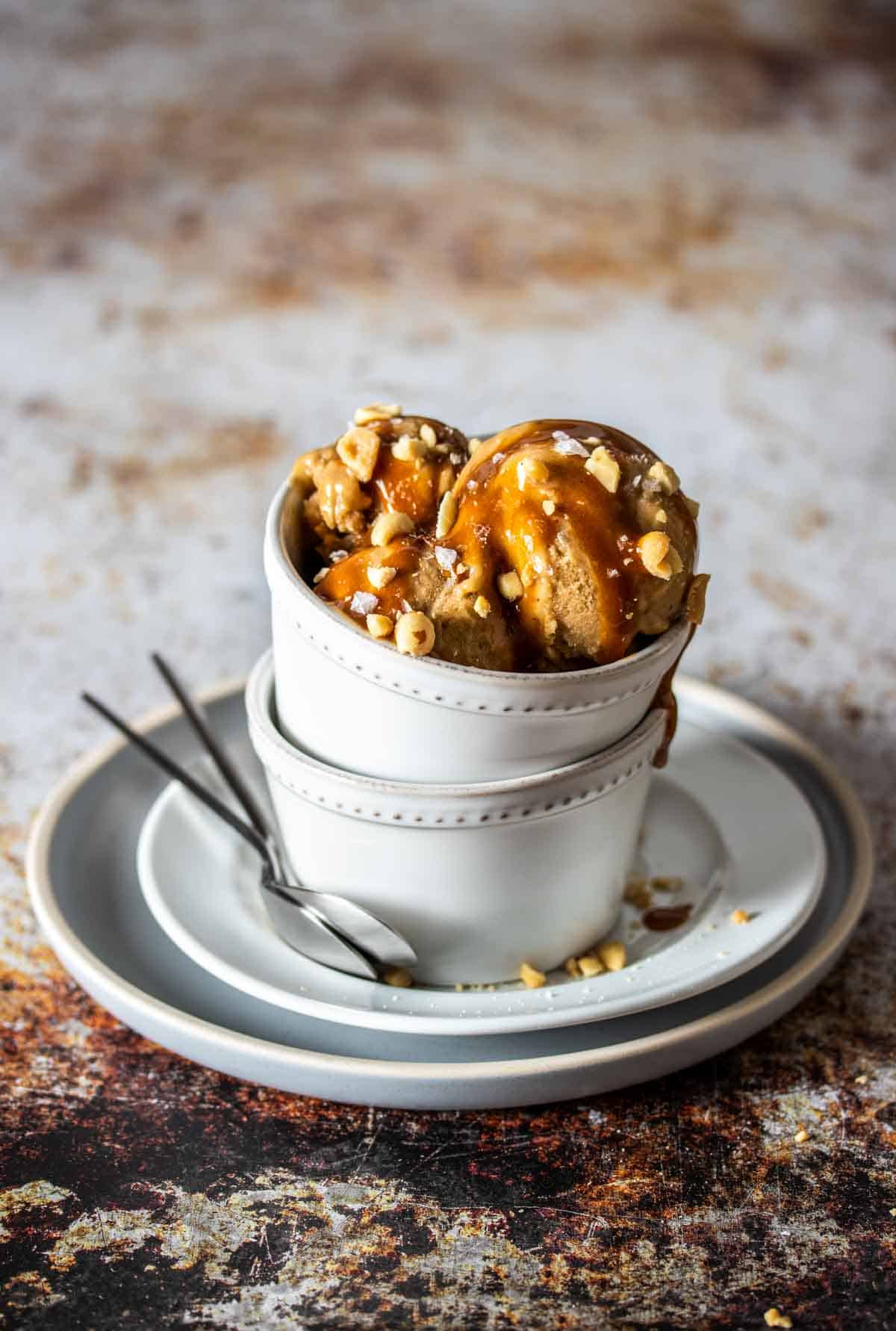 Two white plates stacked and two white bowls stacked on top of them with scoops of peanut butter ice cream inside.