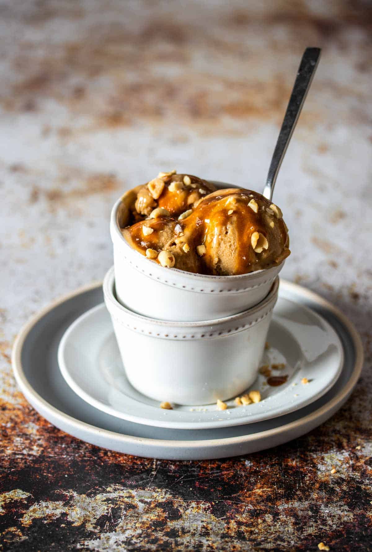 A spoon in a white bowl filled with peanut butter ice cream scoops topped with caramel and peanuts.