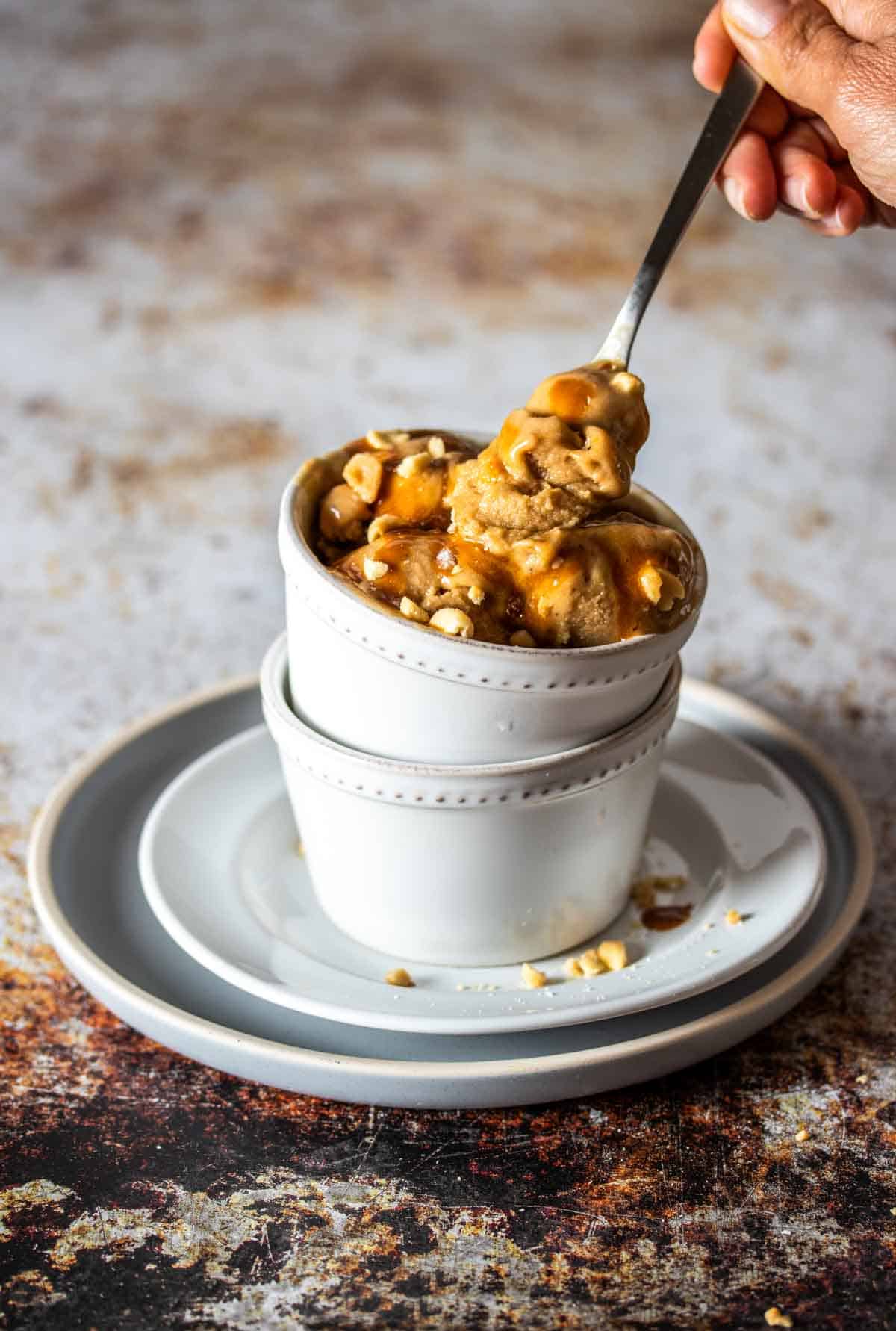 A spoon getting a bite of peanut butter ice cream from a white bowl stacked on another white bowl.