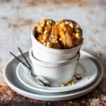 Scoops of a tan ice cream topped with caramel and peanuts in two stacked white bowls on stacked white plates.