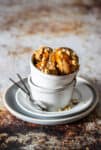 Two white bowls stacked on each other with a tan ice cream topped with caramel and peanuts.