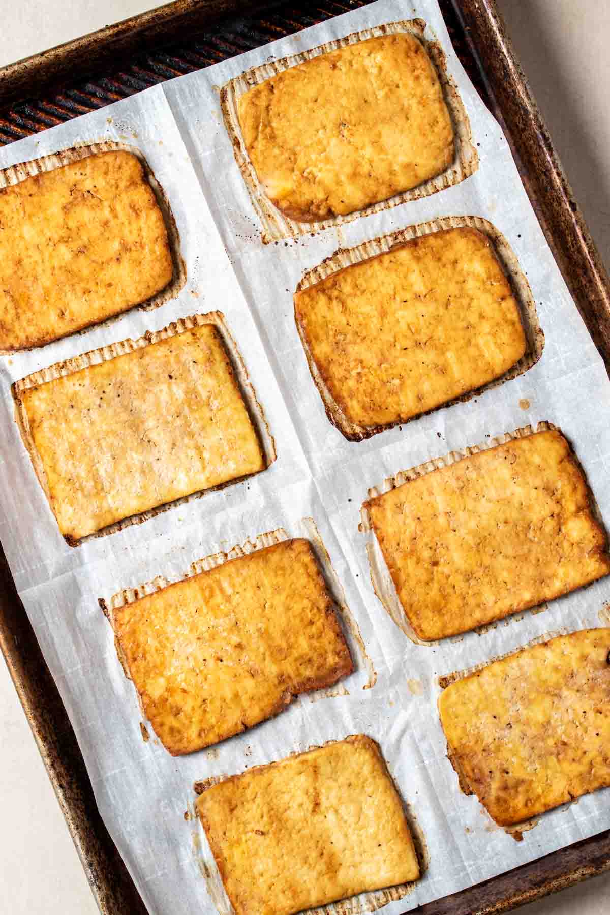 Top view of a parchment lined baking sheet with rectangles of baked thinly sliced tofu on it.