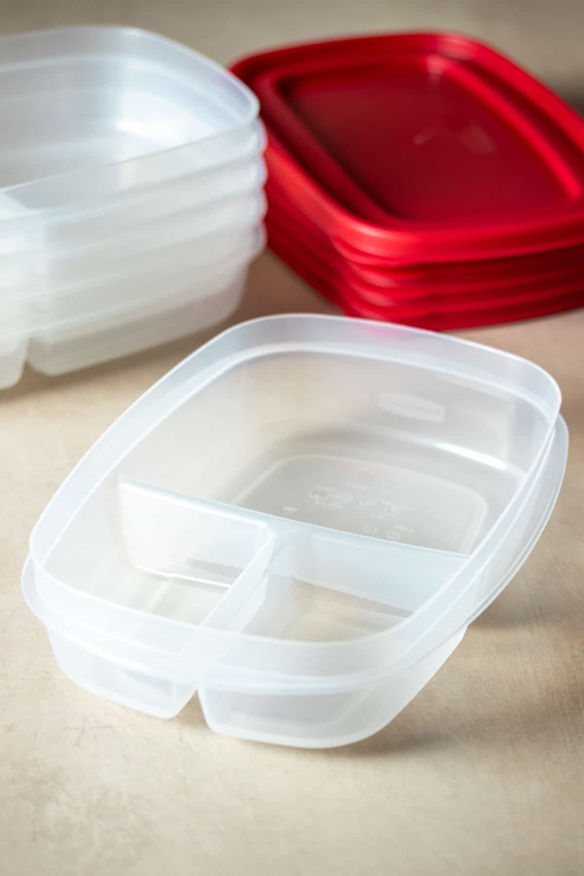 A plastic container with sections in front of a stack of them and a stack of red lids for them.