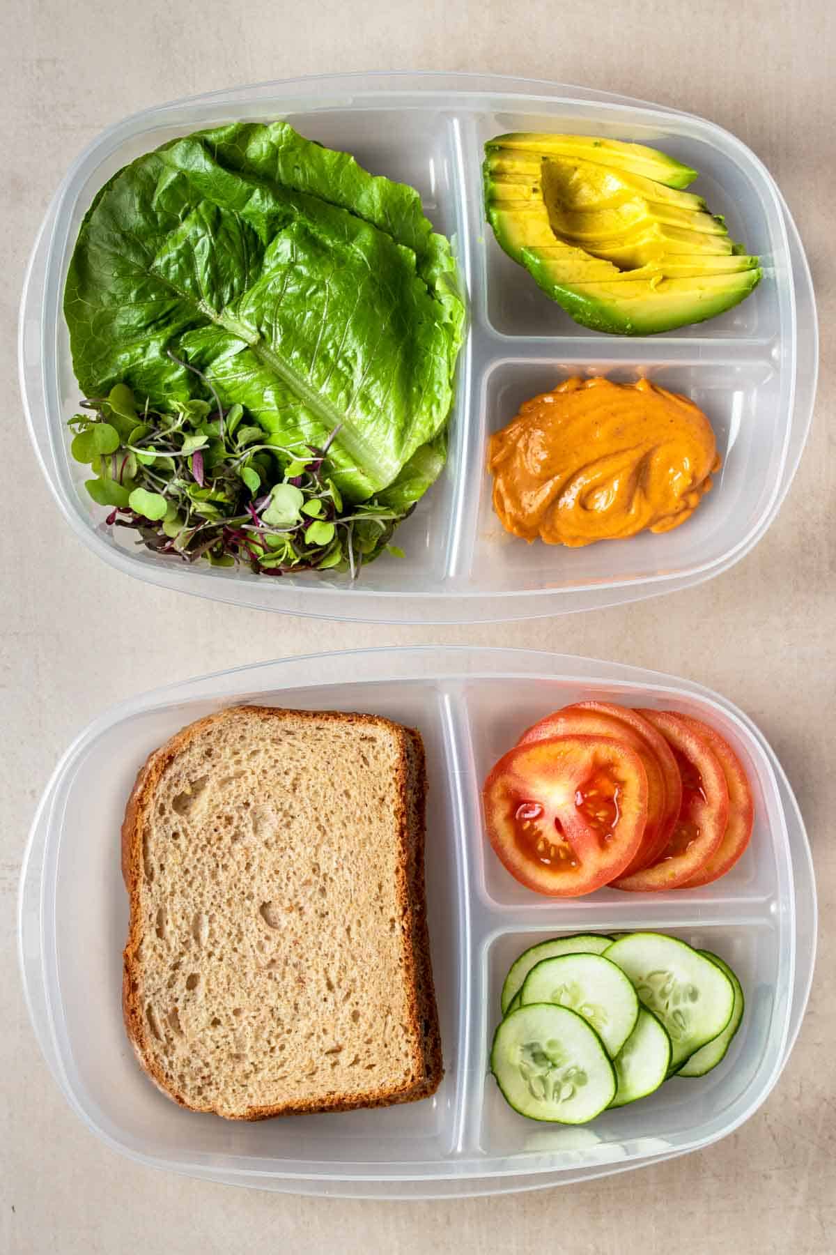 Top view of two plastic containers with sections in them filled with veggies for a sandwich and sliced bread.