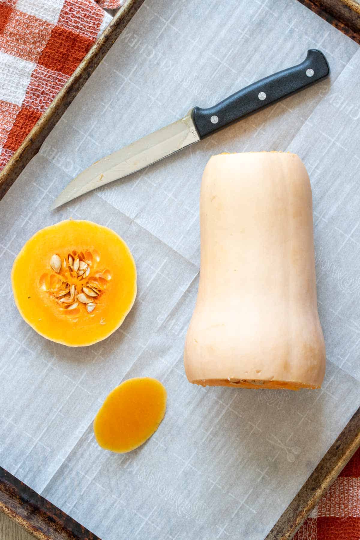 A butternut squash on a parchment lined baking sheet with the top and bottom cut off.