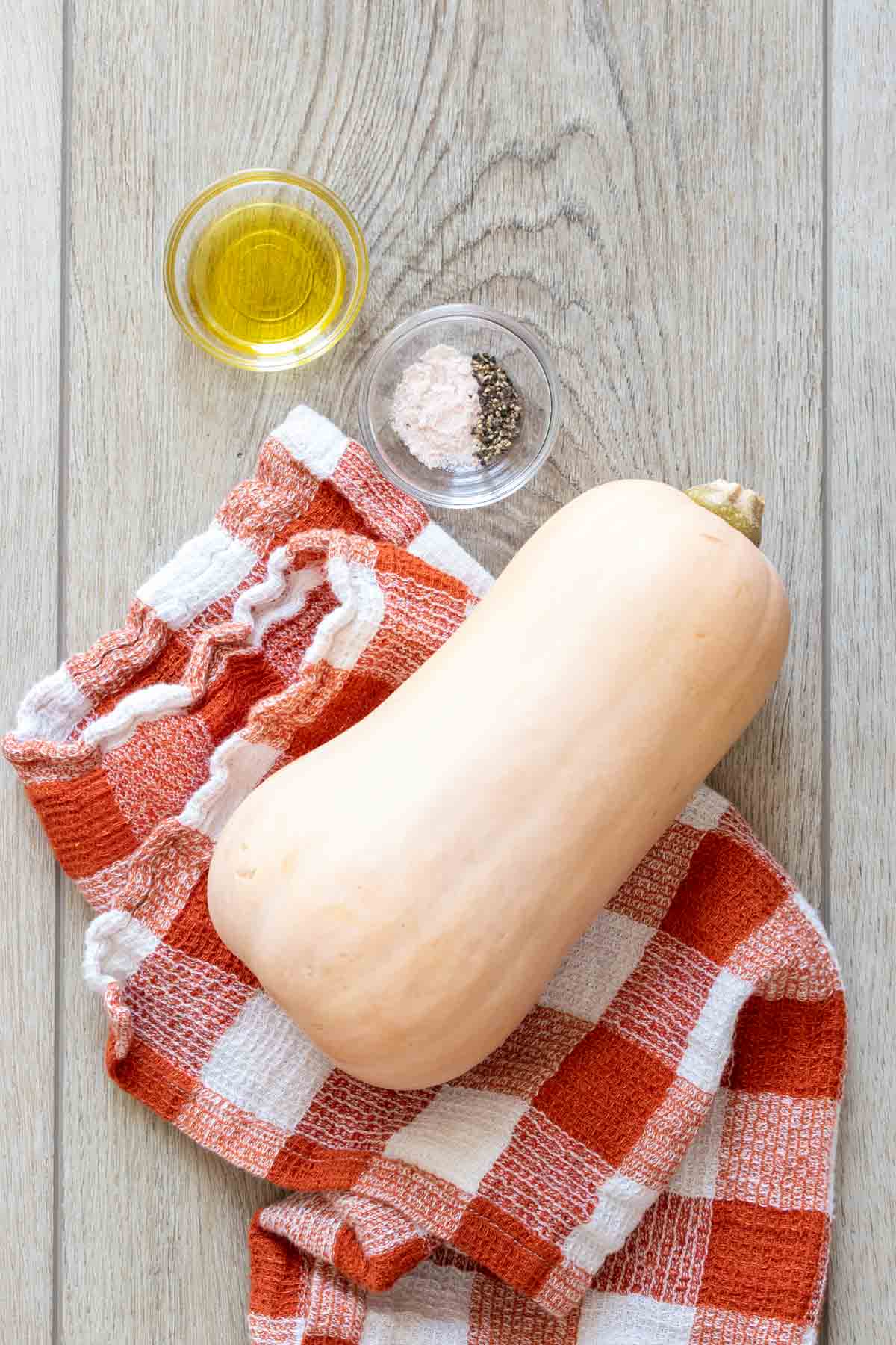 A butternut squash next to two glass bowls of oil and salt and pepper.