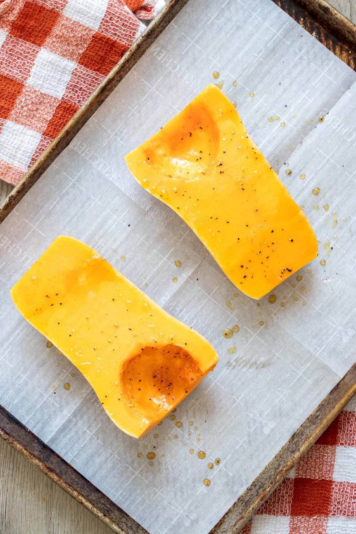Two halves of a butternut squash brushed with oil, salt and pepper on a baking sheet.