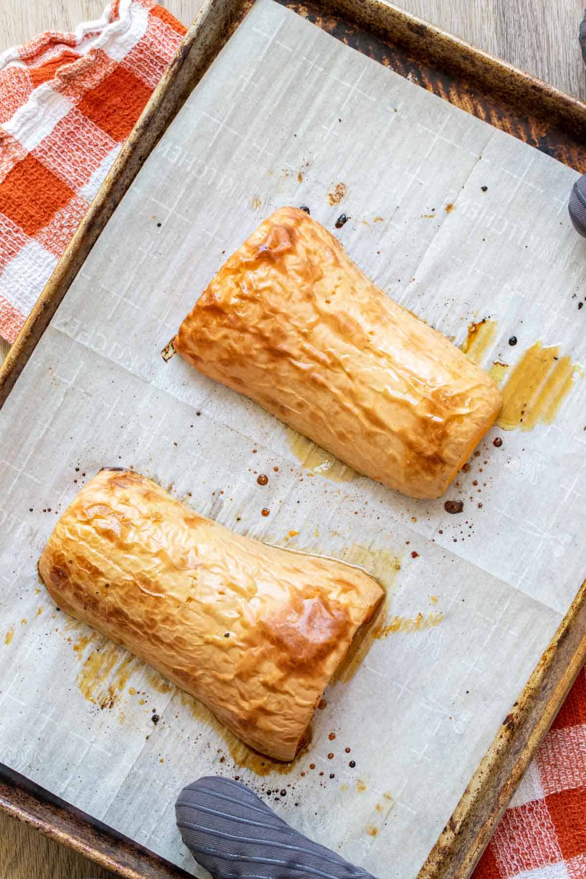 Roasted butternut squash halves face down on a piece of parchment paper on a baking sheet.