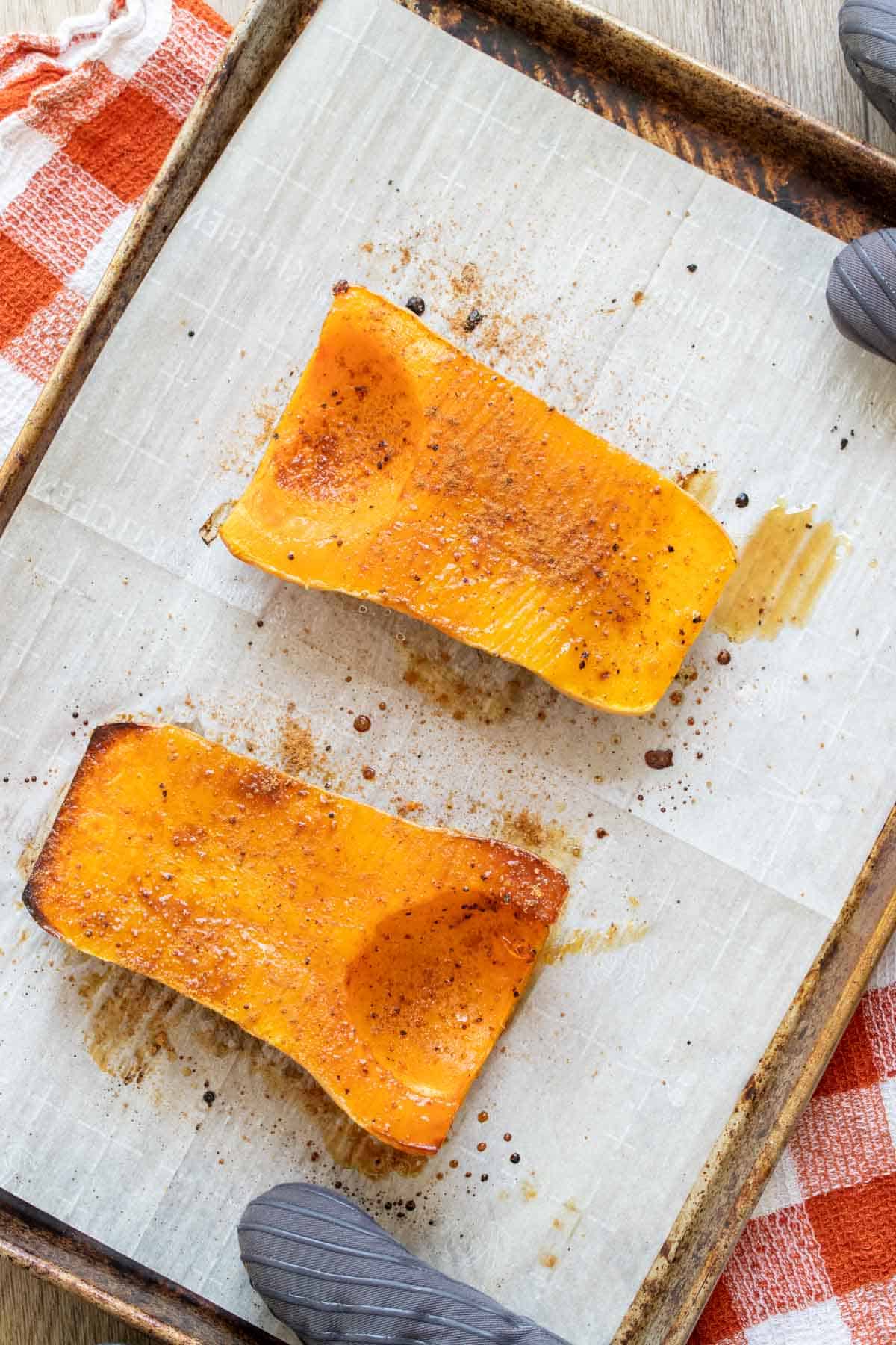 Two halves of butternut squash roasted and sitting face up on a baking sheet.