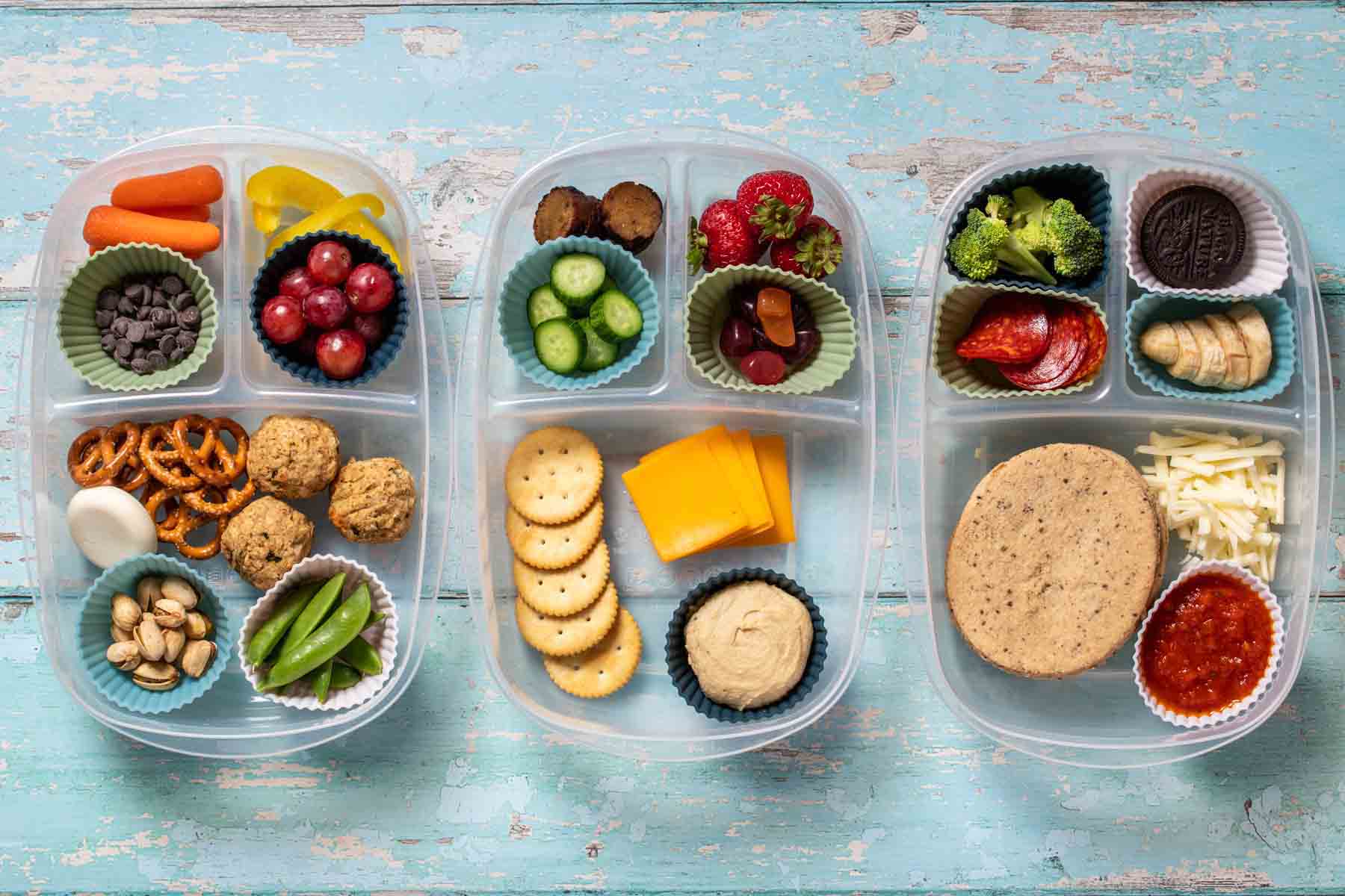 Top view of three different themed homemade lunchables in plastic containers with sections and cupcake liners to hold the different foods.