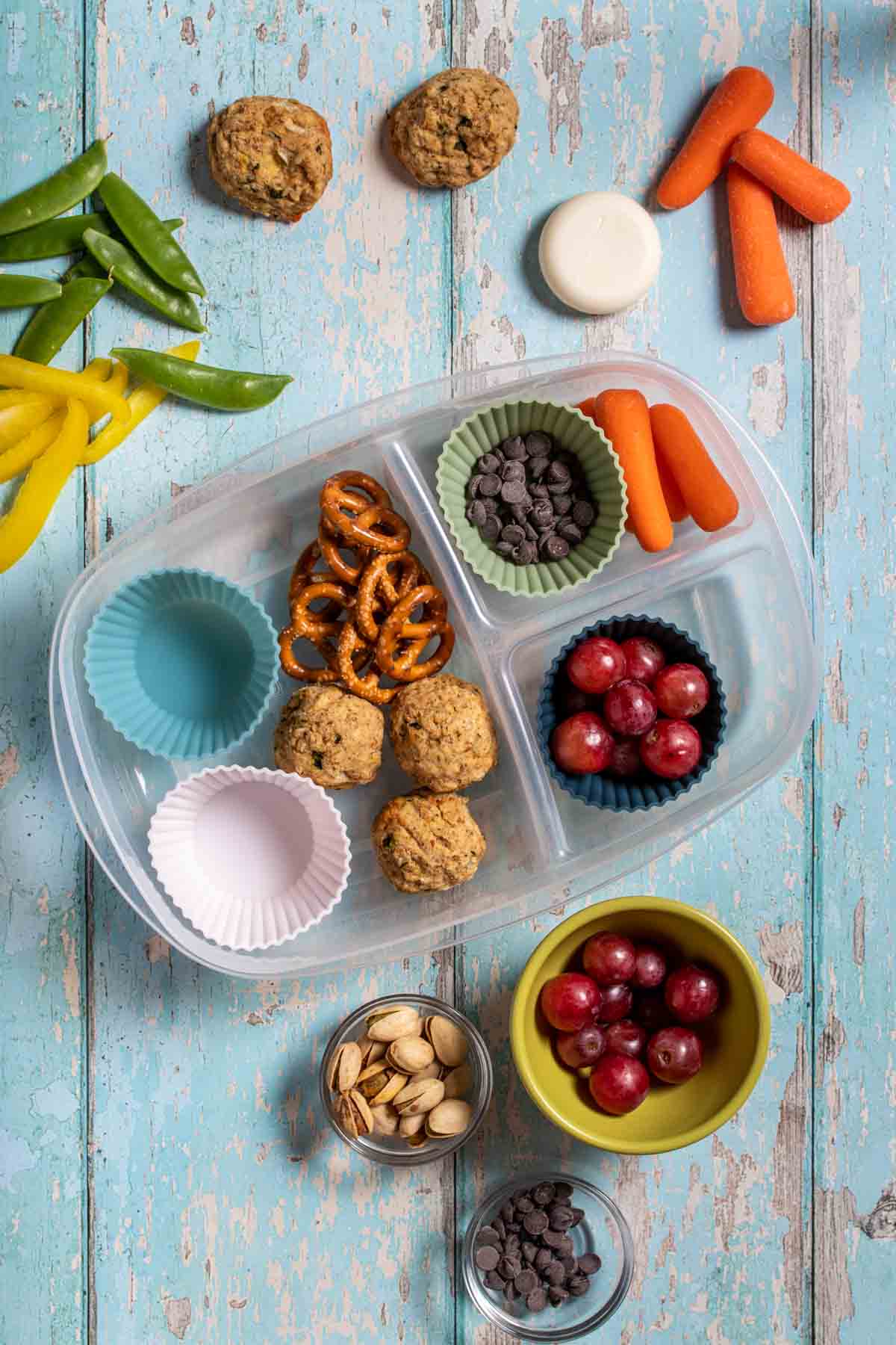 A plastic container with sections and cupcake liners to put in fruit, veggies and snacks with some filled already.