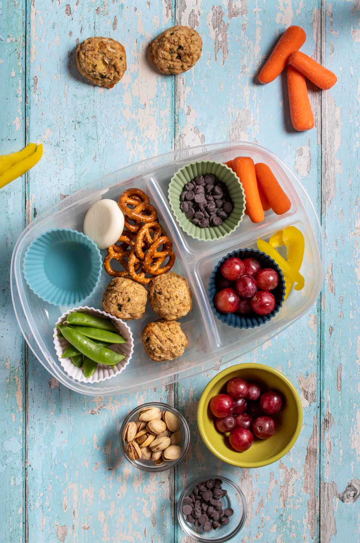 Top view of a homemade lunchable in a plastic sectioned container with fruit, veggies, chocolate chips, pretzels, nuts and protein balls.