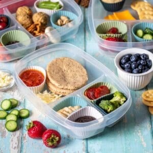 A sectioned container with different food types in each, some in cupcake liners with other containers in the back.