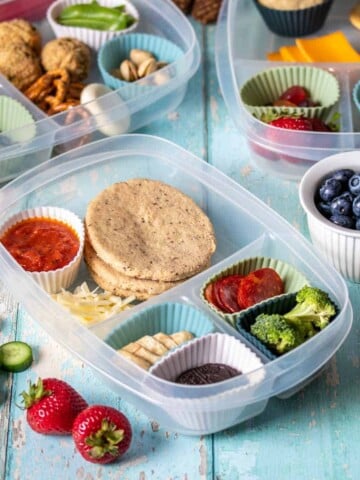 A sectioned container with different food types in each, some in cupcake liners with other containers in the back.