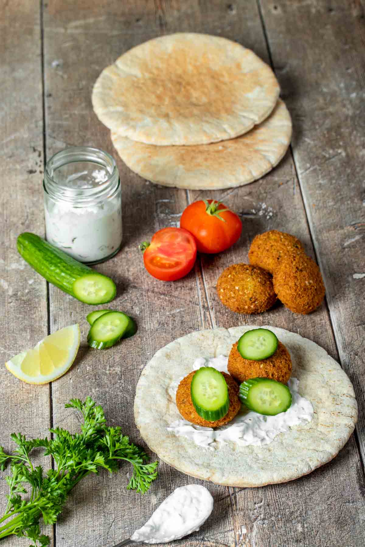 Ingredients to make a falafel sandwich surrounding a pita bread where the sandwich is being built on.