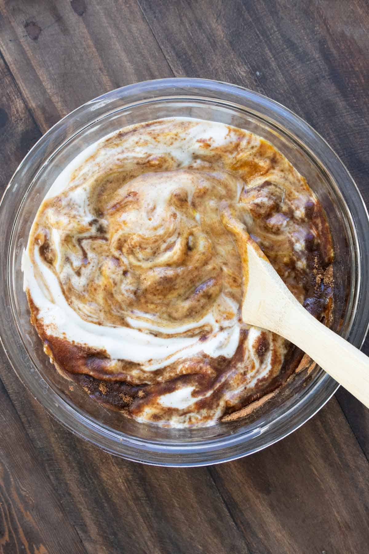 A wooden spoon mixing a brown caramel like batter into whipped cream.