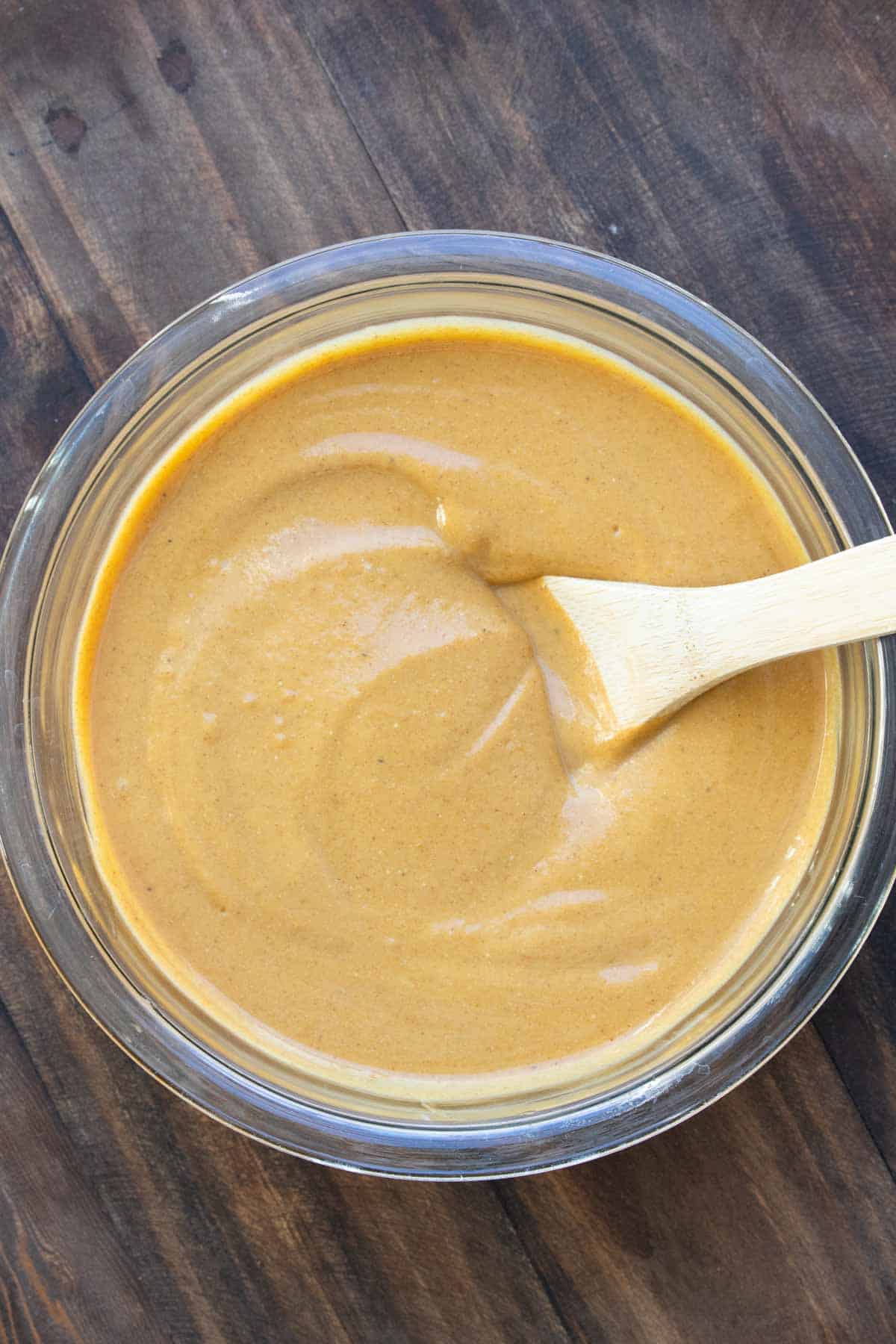 A wooden spoon mixing a creamy pumpkin mixture in a glass bowl.