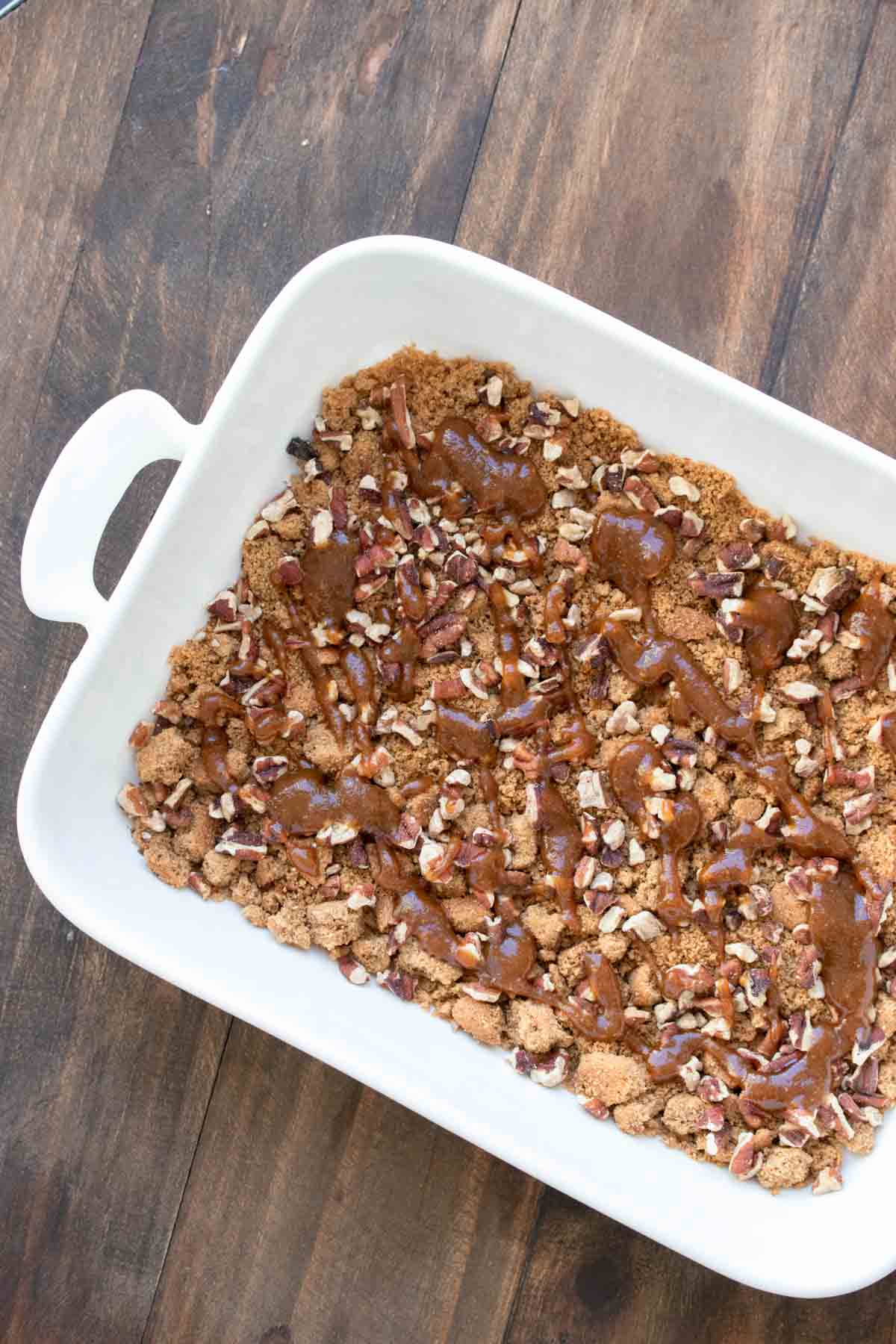 A white baking dish with crushed cookies and pecans and drizzled with a caramel.