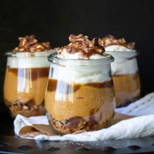 A layered cookie, nut, pumpkin and whipped cream dessert in three glass jars.