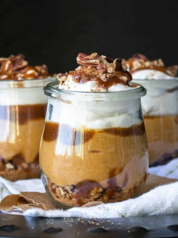 A layered cookie, nut, pumpkin and whipped cream dessert in three glass jars.