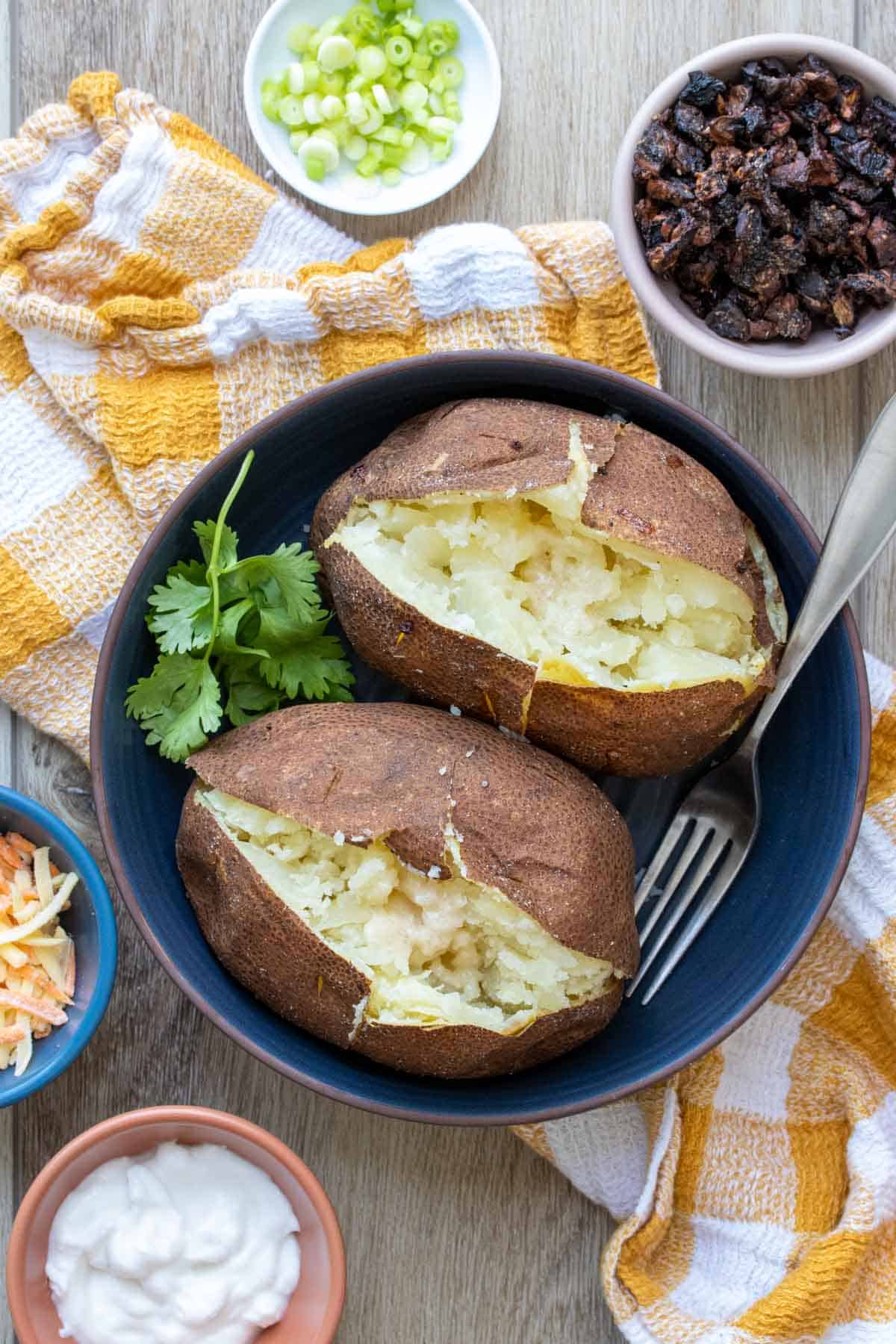 Two potatoes that have been baked and cut open on the top sitting in a dark blue shallow bowl.