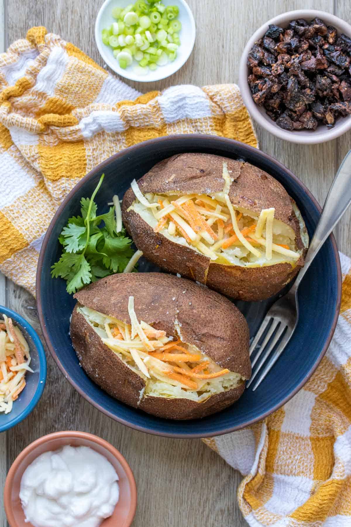 A shallow blue bowl with two baked potatoes cut open and topped with shredded orange and yellow cheese.