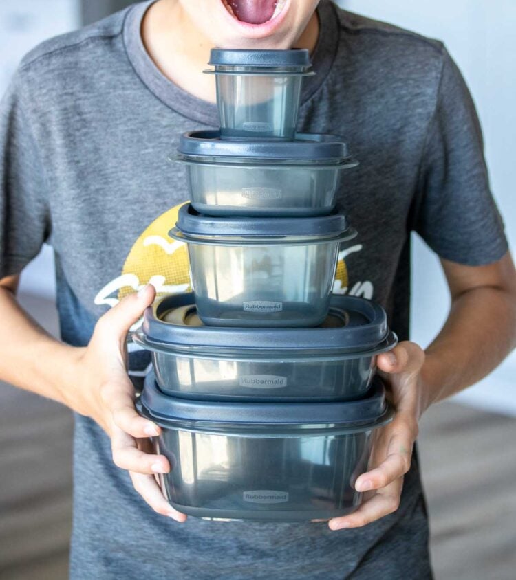 A boy with a shocked expression holding a stack of five different sized containers in size order in his hands.